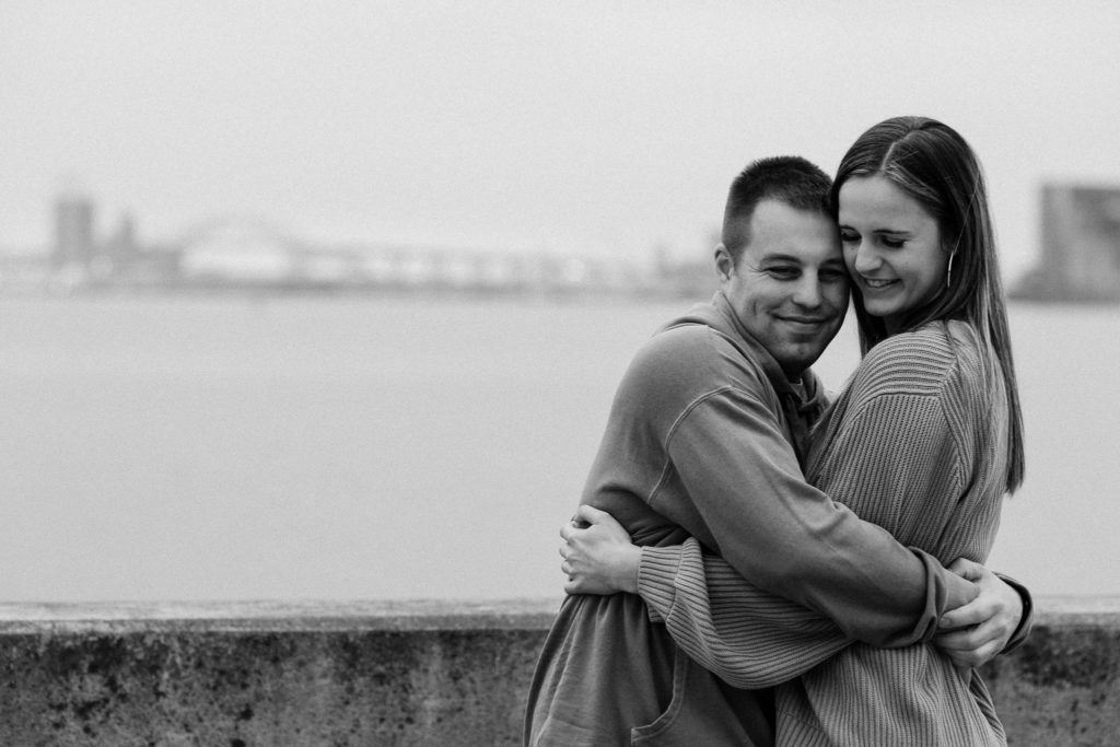 Black and white photo of couple hugging with the cityscape in the background.