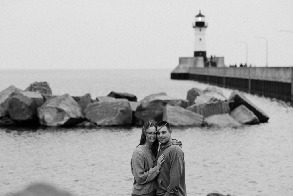 Series of black and white photos of couple embracing in front of the lighthouse and shoreline in Canal Park, Duluth MN