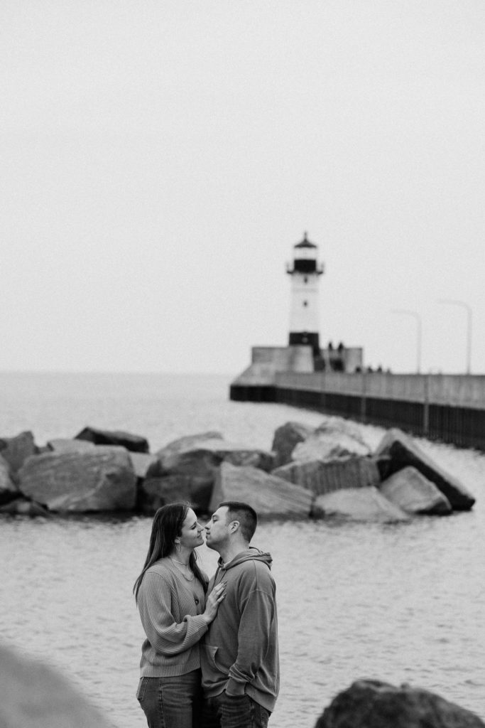Black and white photo of couple kissing among the rocks and shoreline in Duluth MN