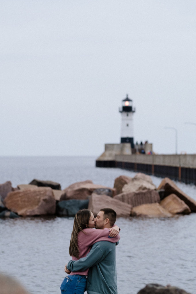 Couple kissing with the lighthouse and shoreline in the background. Canal Park Duluth MN
