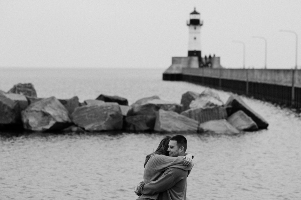 Series of black and white photos of couple embracing in front of the lighthouse and shoreline in Canal Park, Duluth MN