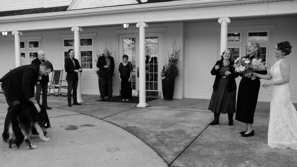 Black and white image of all wedding couple and their family standing outside laughing and enjoying each other's company in front of the Oakwood Inn at Okoboji.