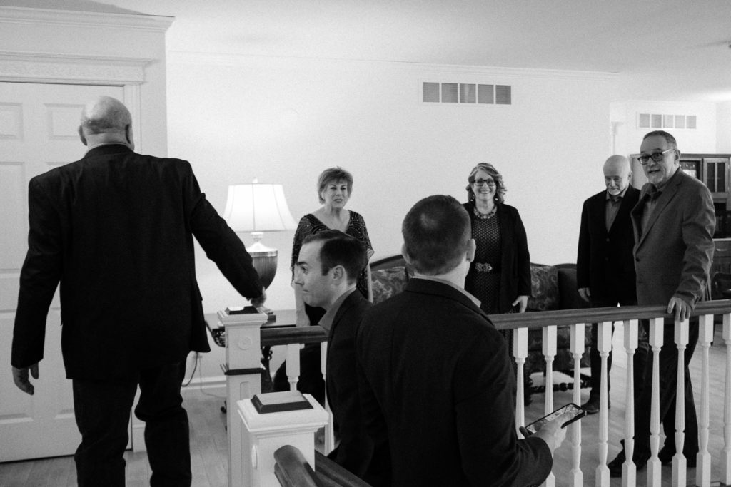 A black and white image of the bride and groom's family standing together waiting to walk down the stairs and into the ceremony space. 