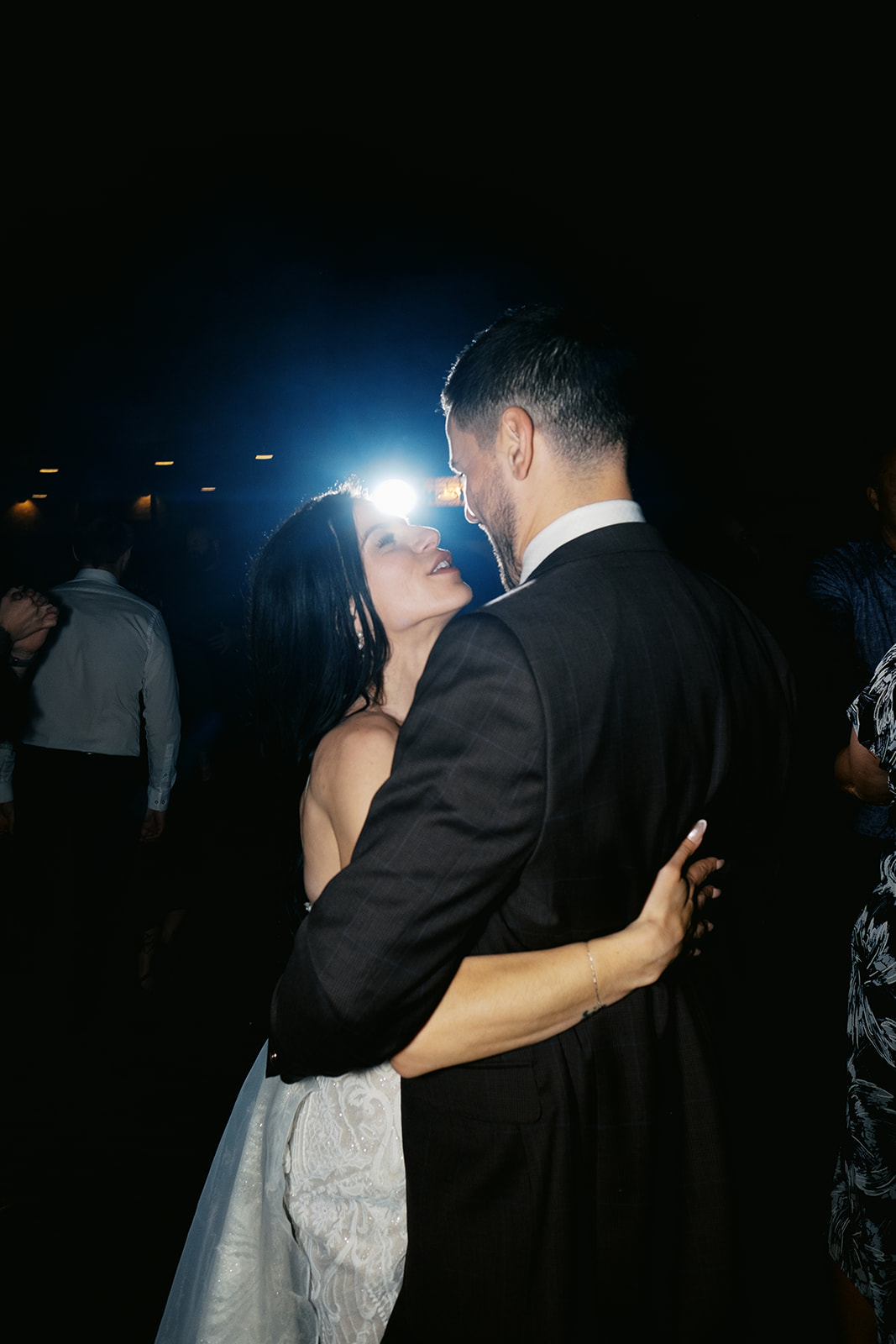 Megann and Carl are dancing on a dark dance floor, gazing into each other's eyes, illuminated by a flash of blue DJ lights and direct flash from the wedding photographer.