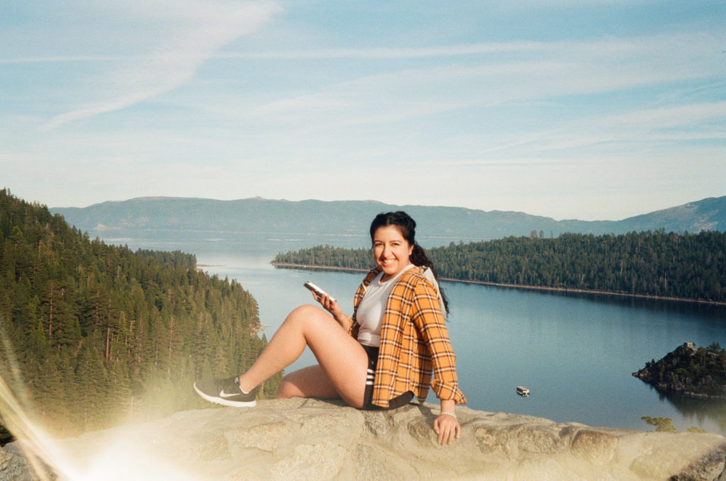 Color film photo of Ada sitting on a ledge over looking Lake Tahoe from Emerald Bay State Park. There's a light leak in the lower portion of the frame.