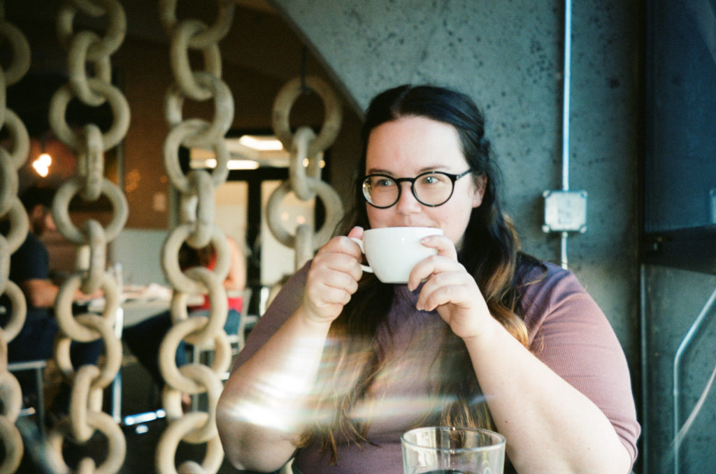 A color film photo of Ashley drinking coffee in a chic restaurant/cafe in Reno.