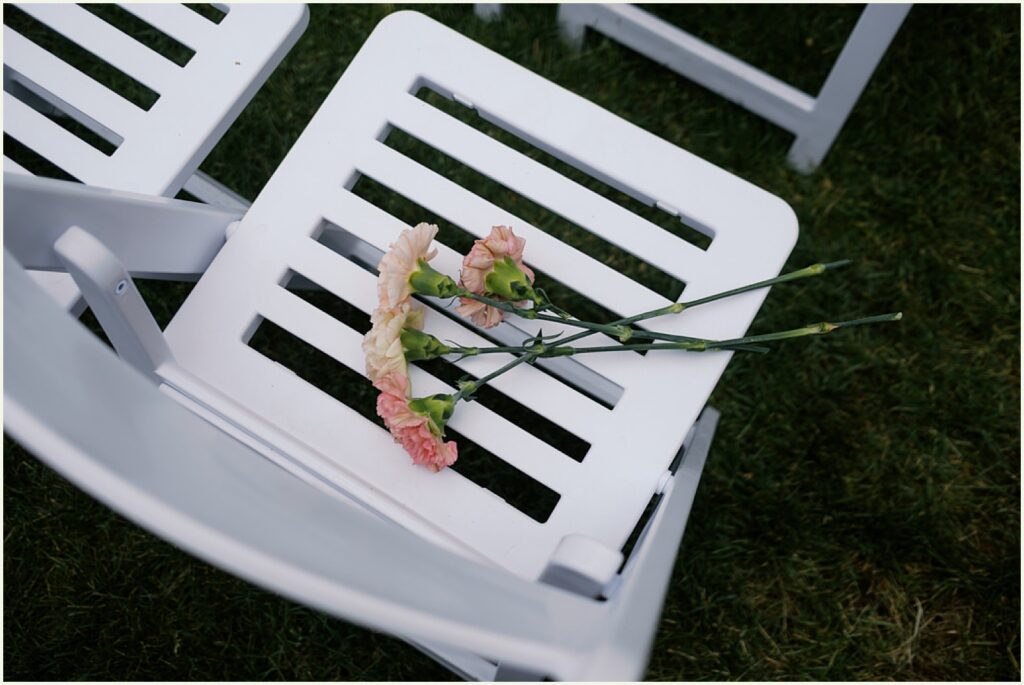 Pink flowers sit on a chair before an outdoor wedding ceremony.