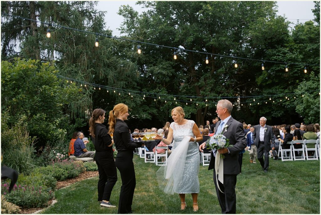 A bride's parents approach a server holding a tray of wine glasses at the An Elegant Wedding at the St. Paul University Club.
