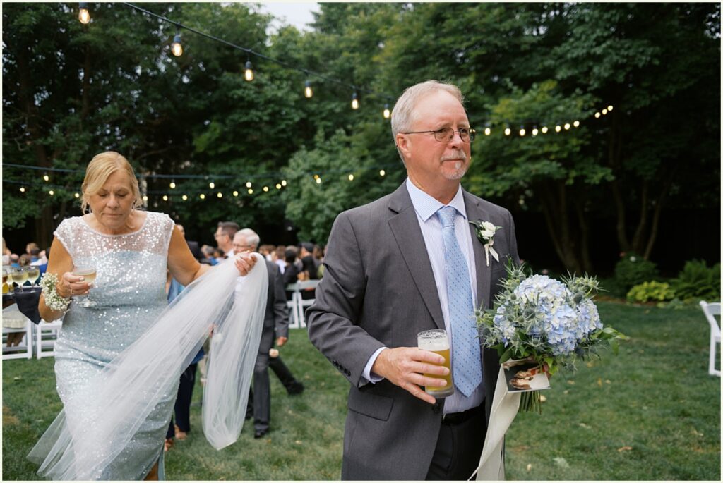 A bride's father carries her bouquet, and her mother carries her veil.