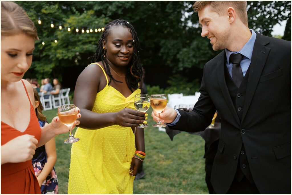Two wedding guests clink glasses on a lawn.