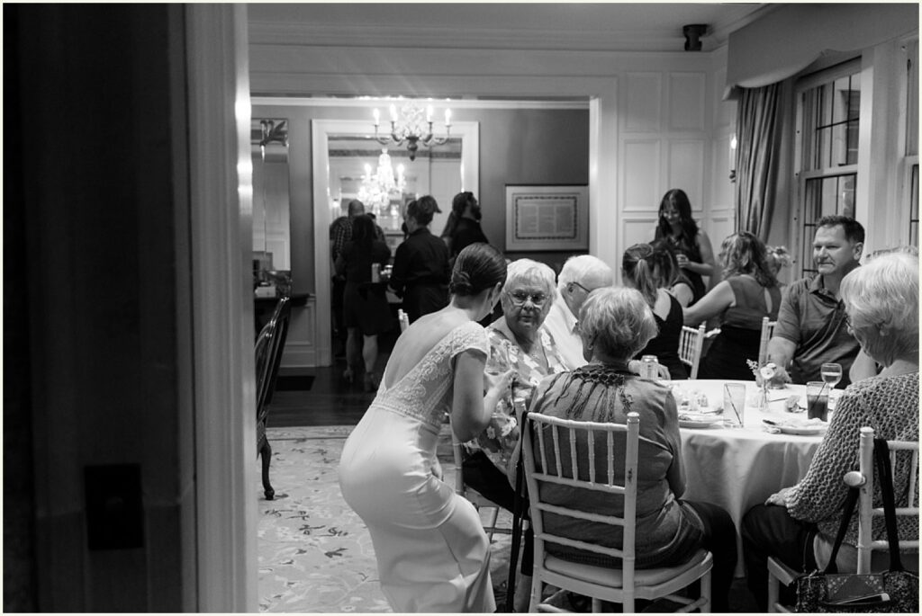 A bride stoops to speak with wedding guests at reception tables in the An Elegant Wedding at the St. Paul University Club.